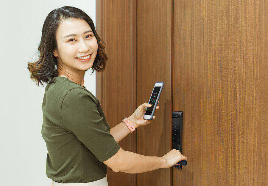 Smiling women unlocking hafele digital door lock with help of mobile phone app